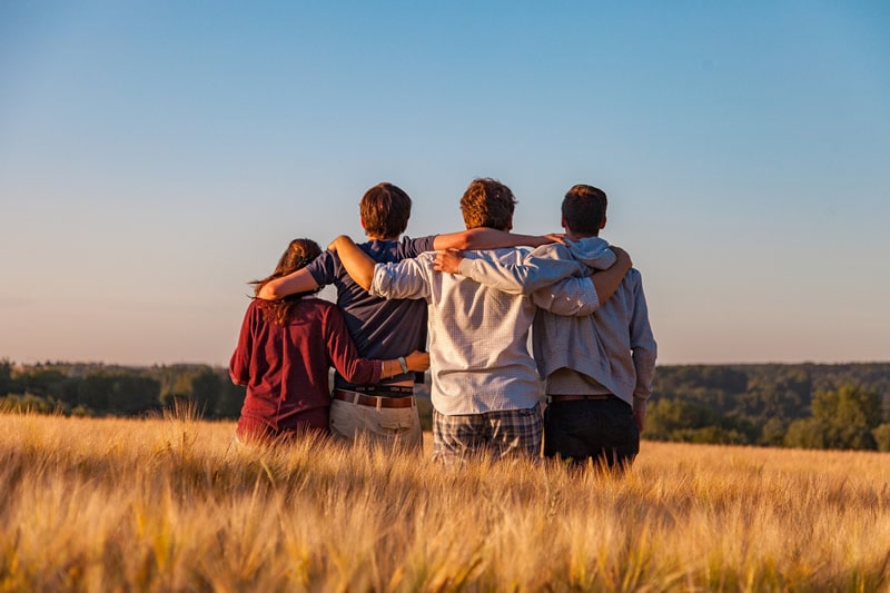 Eine Gruppe junger Leute von hinten im Feld sitzend.
