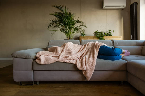 Eine Frau verkriecht sich unter der Decke auf einer Couch.