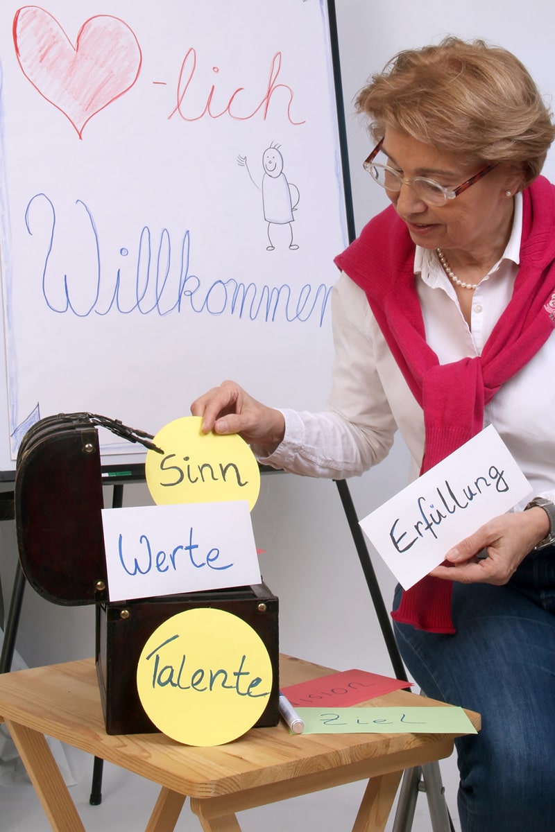 Daniela Sander-Lehmann hält die auf Karton geschriebene Begriffe Sinn, Werte, Talente, Erfüllung hoch.